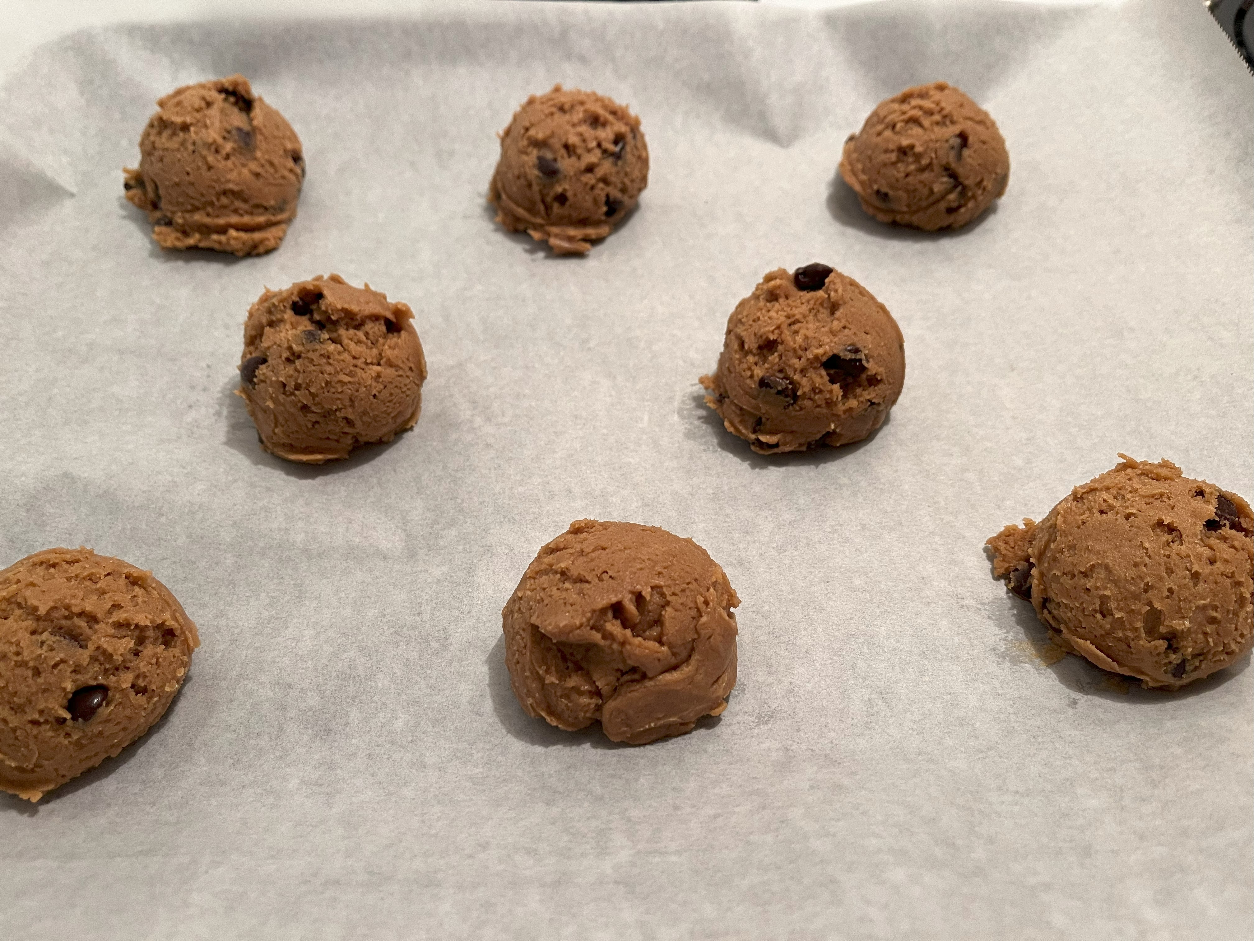 Cookie dough balls on a parchment paper-lined baking sheet.