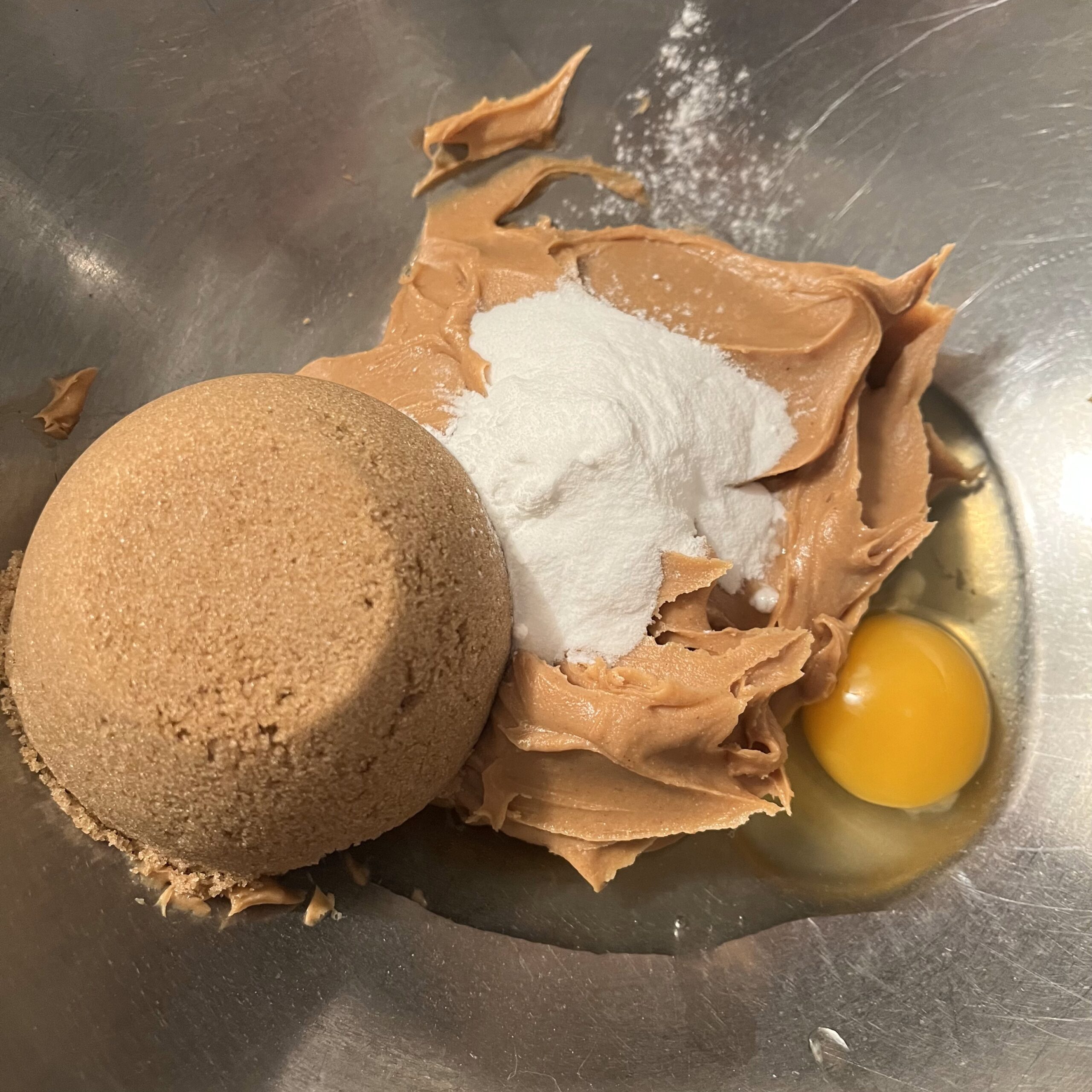 Ingredients (peanut butter, baking powder, baking soda, an egg, brown sugar) in a mixing bowl.