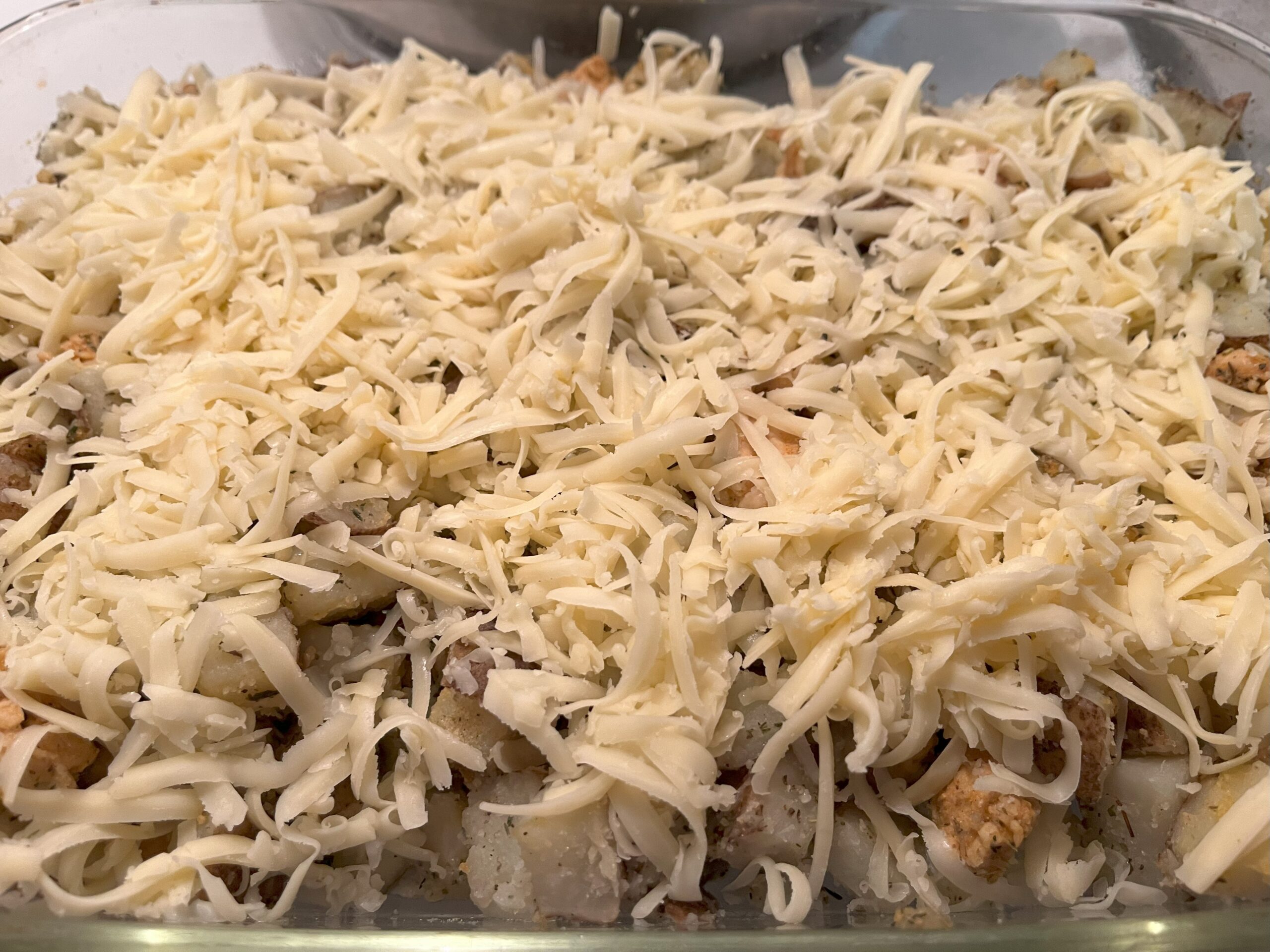 Assembling the casserole — cheese is added on top of the chicken and potatoes.