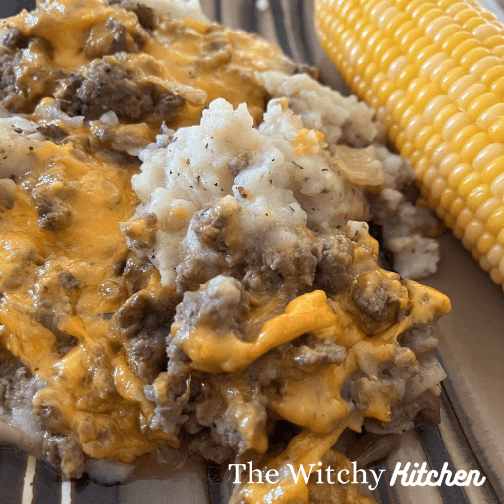 Beef and Potato Gratin on a plate with corn on the cob by The Witchy Kitchen.