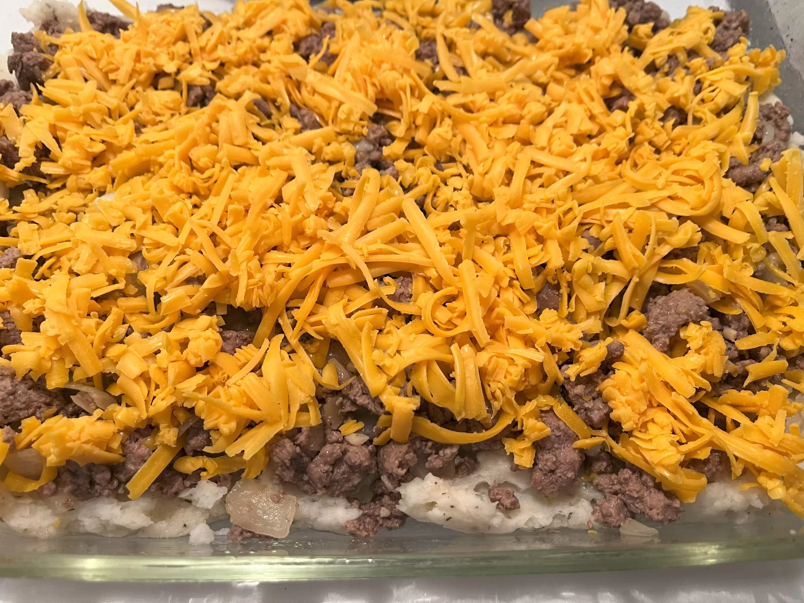 Grated cheese on top of beef, onions, garlic, and potatoes.