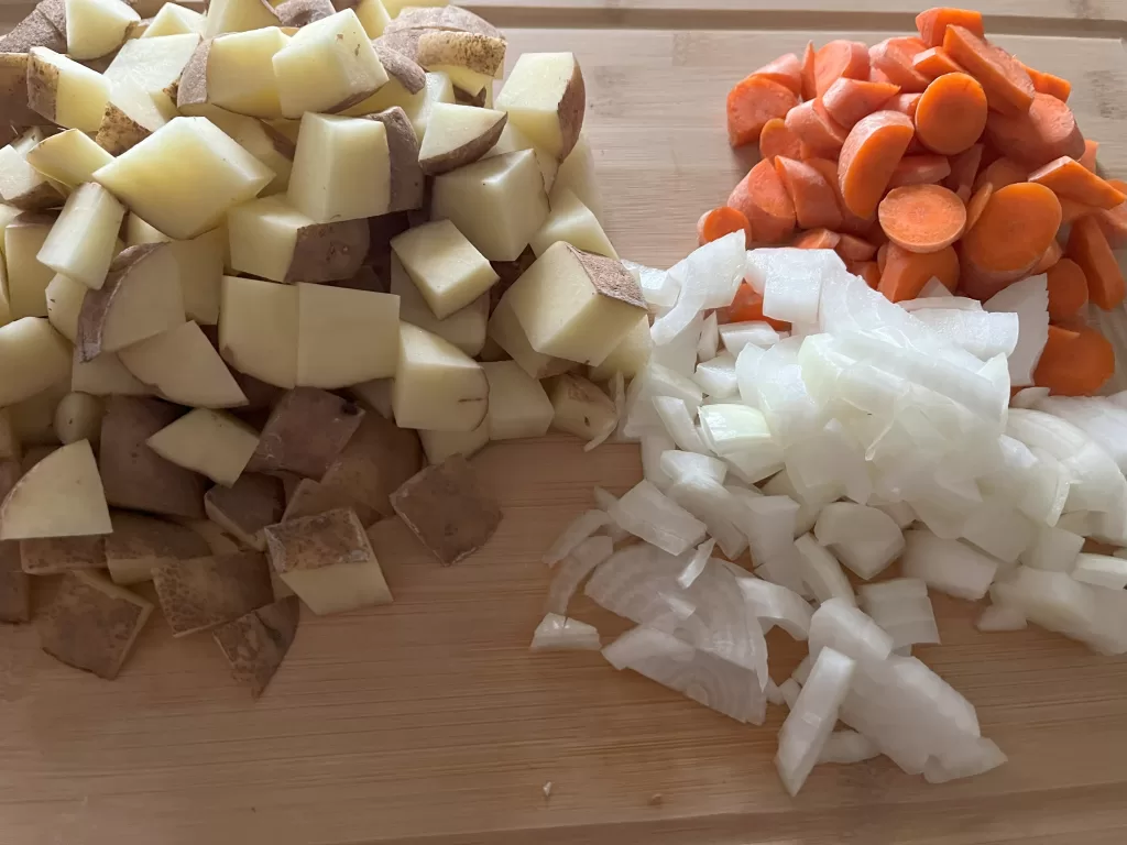 Potatoes, carrots, and diced onion on a cutting board.