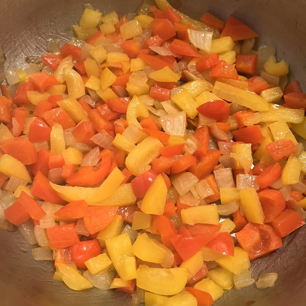 Diced bell peppers and onion cooking in a pot.