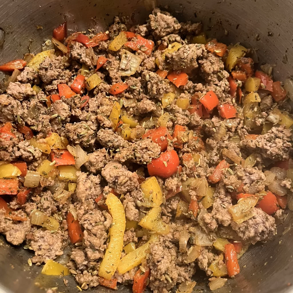 Bell peppers, onions, ground chicken, herbs, and spices in a pot.