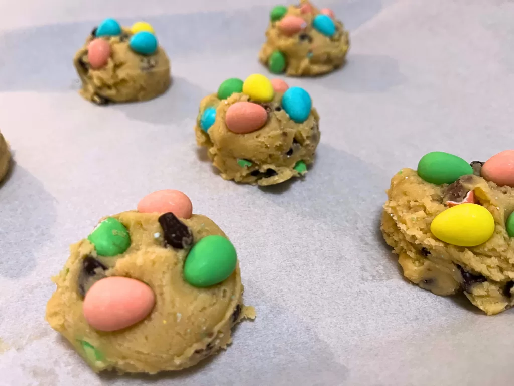 Close up of Mini Egg cookie dough balls on a parchment paper-lined baking sheet.