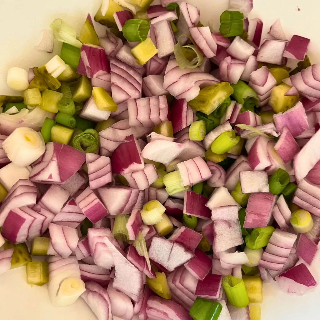 Red onions, green onions, and pickles in a white bowl.