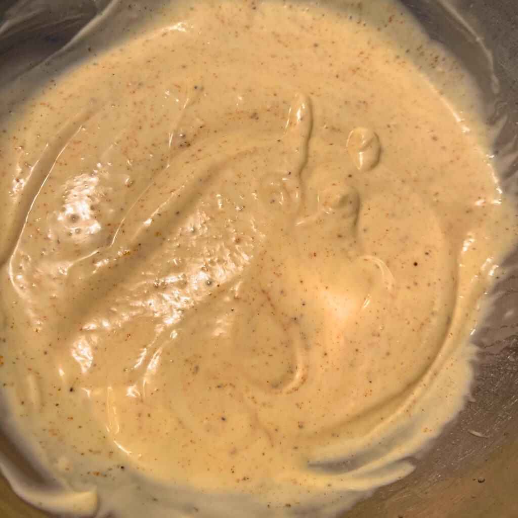 A yellow-white dressing with speckles of spice made of mayonnaise, sour cream, Dijon mustard, pickle juice, sugar, and spices (salt, pepper, garlic powder, paprika).