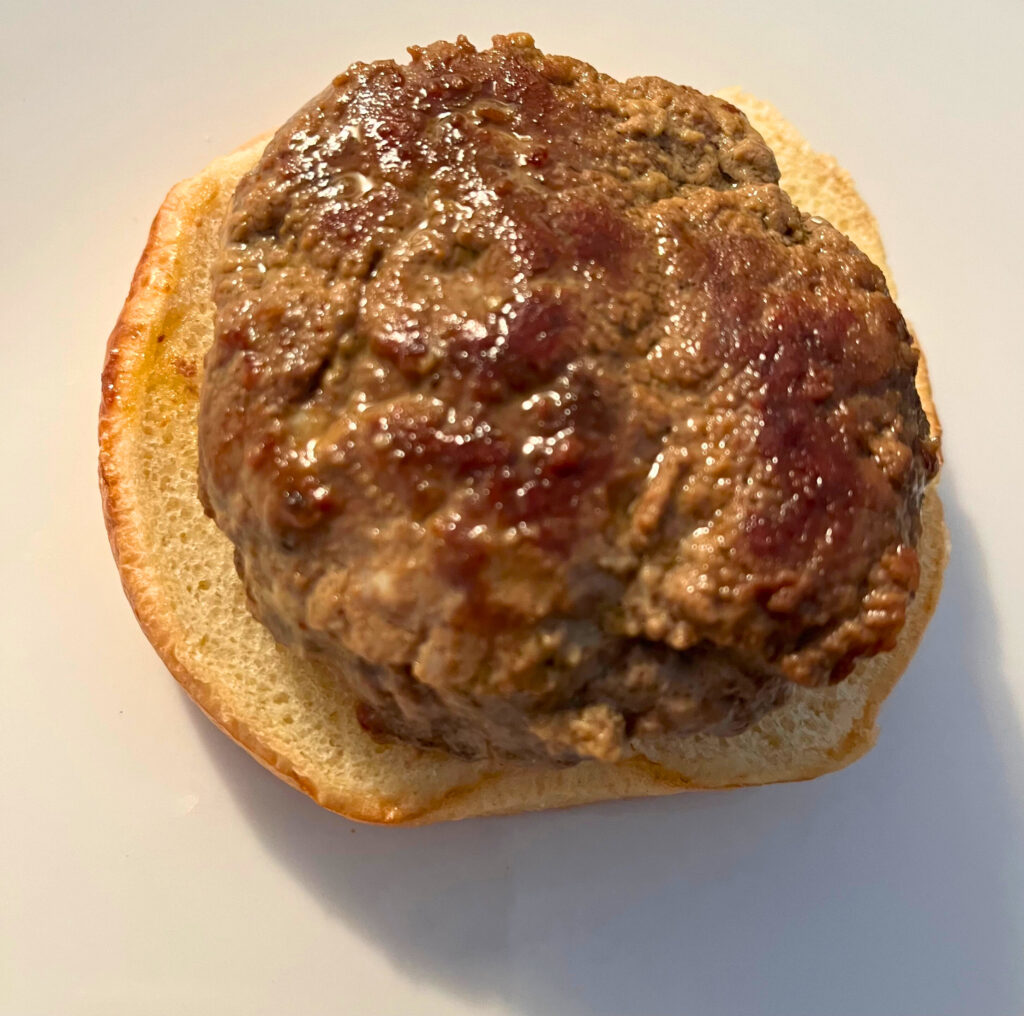 A cooked hamburger patty on top of a bun, on a white plate.