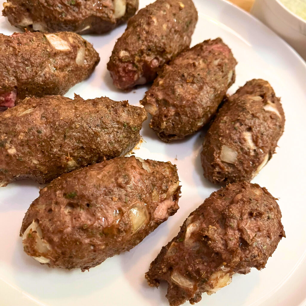 Chicken kofta kebabs on a white plate with a white bowl of garlic-yogurt sauce slightly visible in the top right corner