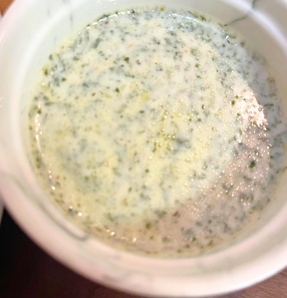 Garlic-yogurt sauce with parsley and dill in white bowl.