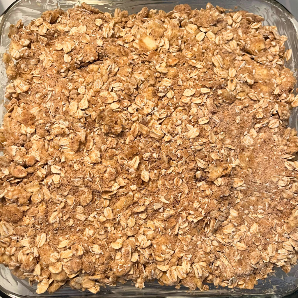 Crisp topping, made from butter, oats, flour, brown sugar, salt, cinnamon, nutmeg, and ginger, in a greased clear glass baking dish.