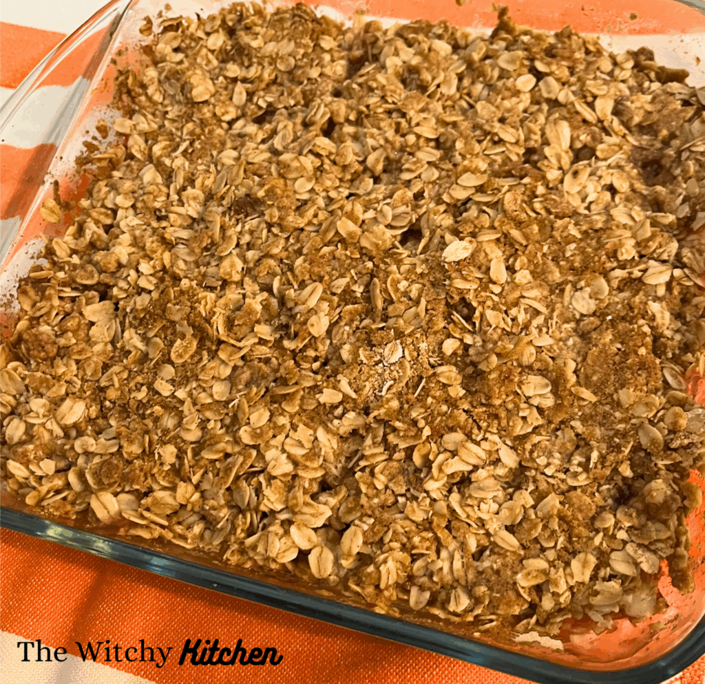 Rhubarb crisp with visible oats and brown topping in a clear glass baking dish on top of an white and orange striped towel.